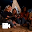 six people sitting on the beach and one girl is holding a guitar