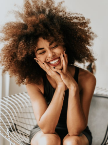 Black woman with an afro hairstyle laughing with her eyes closed